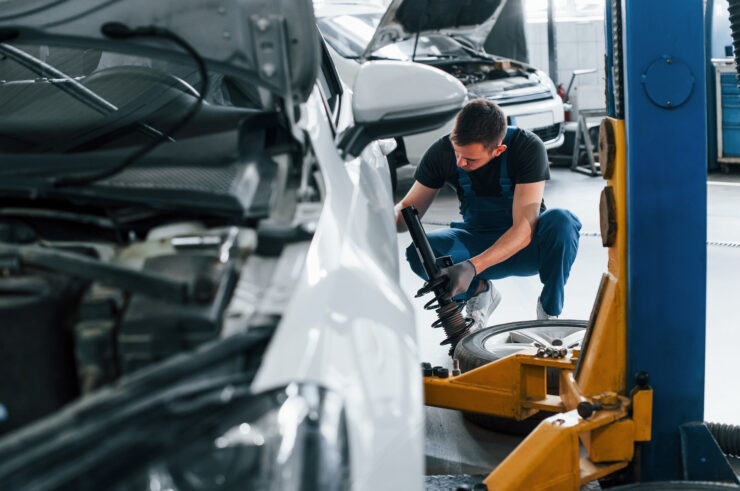 Auto mechanic performing collision repair process by inspecting and replacing a car suspension part in a professional auto body shop.