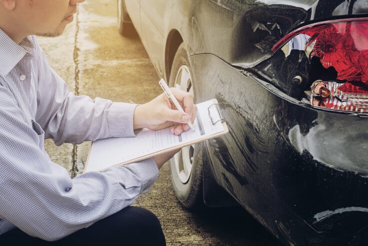 Technician inspecting rear-end vehicle damage while preparing a collision repair estimate after a car accident.