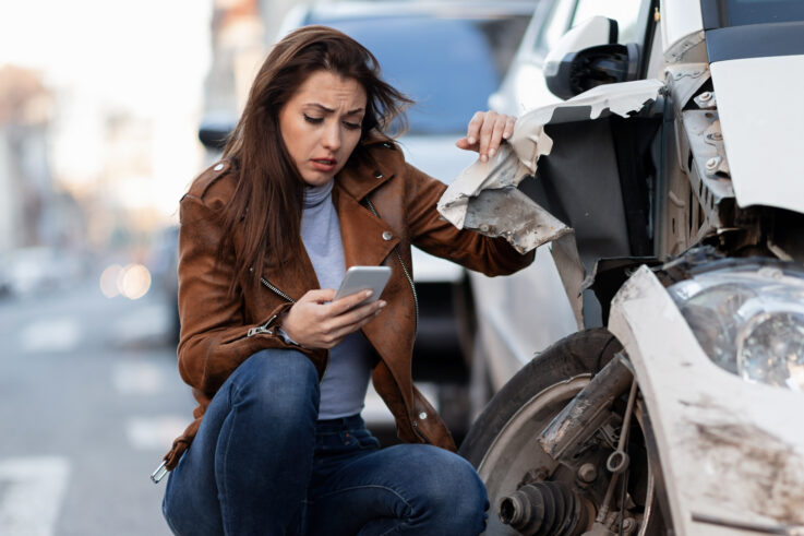 Woman using her phone after a car accident to contact emergency services and insurance.